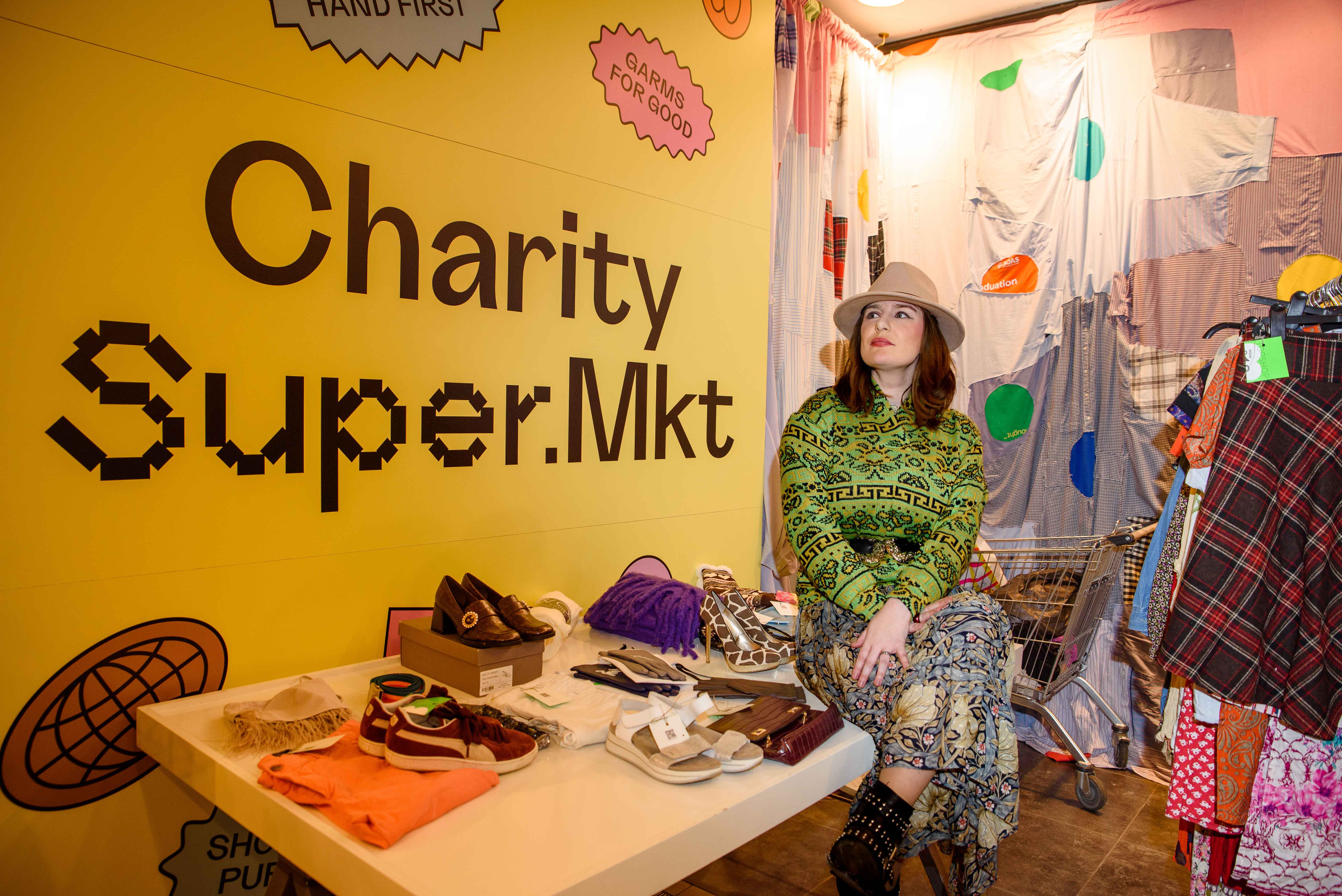 Model sitting inside Charity Super.Mkt store, surrounded by display items